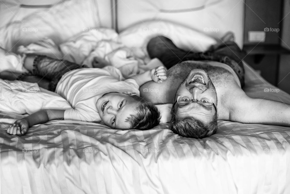 Father and son laying on the bed together. Happy family. Smiling people. Black and white.