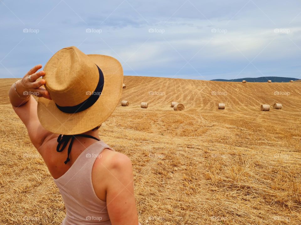 woman from behind with hat walks in a harvested wheat field