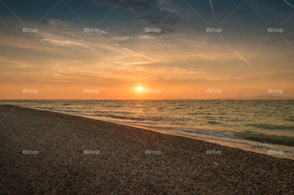 Sunset over pebble beach on Island of Rhodes at Aegean sea. Mediterranean sea. Greece. Europe.