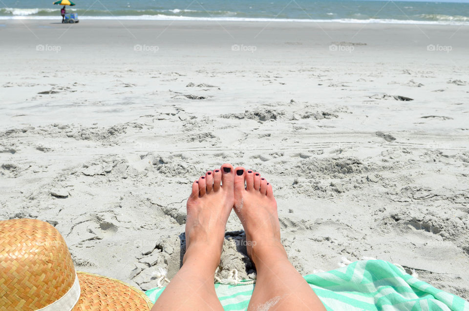 First person point of view of woman's feet in the sand at a beach with view of the ocean