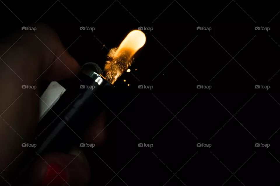 A person has lighters in his hands and he lights it through a flint wheel, the lighter ignites, sparks and fire appear, close-up on a black background.