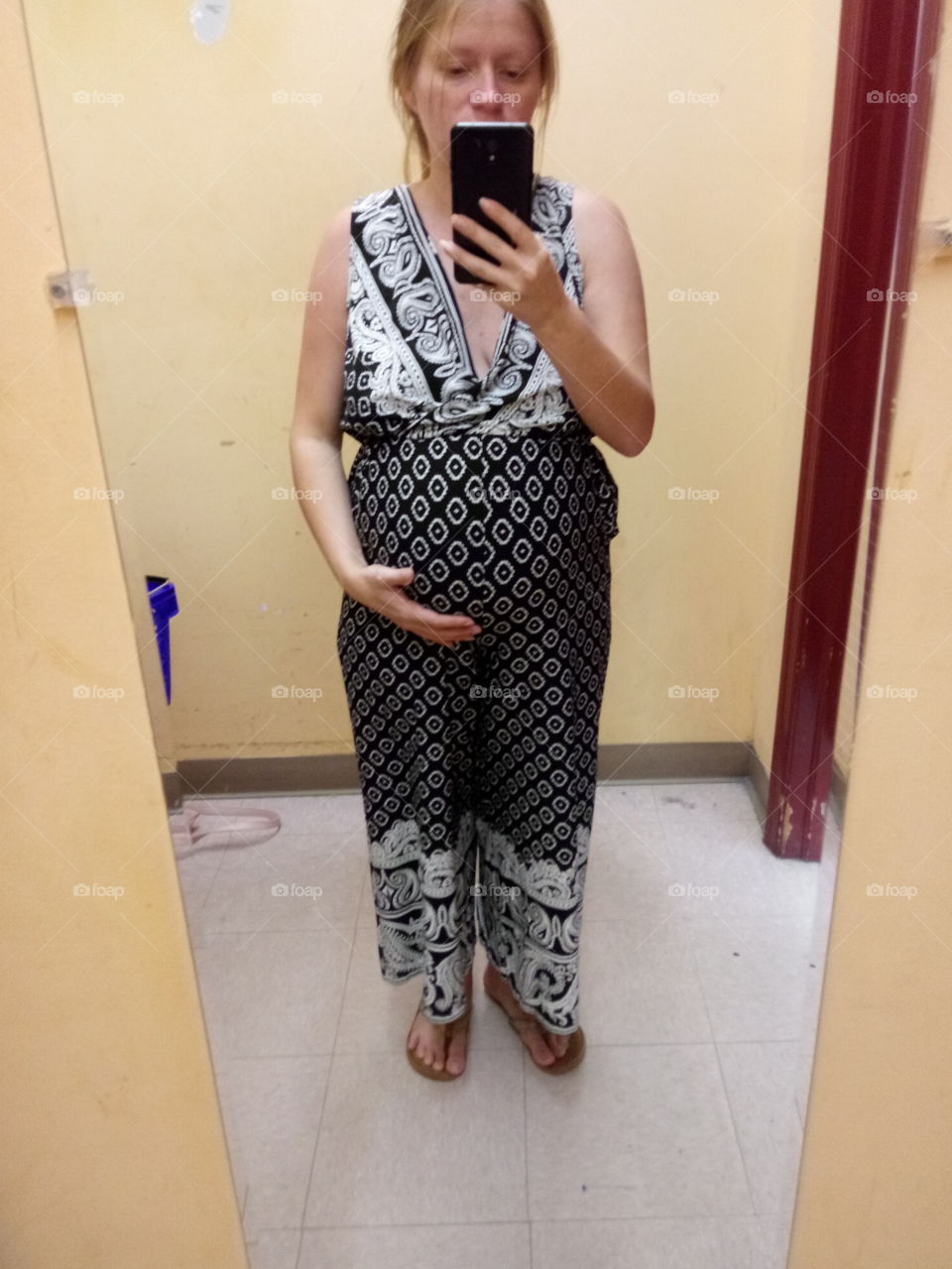 a new mom taking a picture of her baby bump in the mirror of a fitting room while trying on maternity clothea.