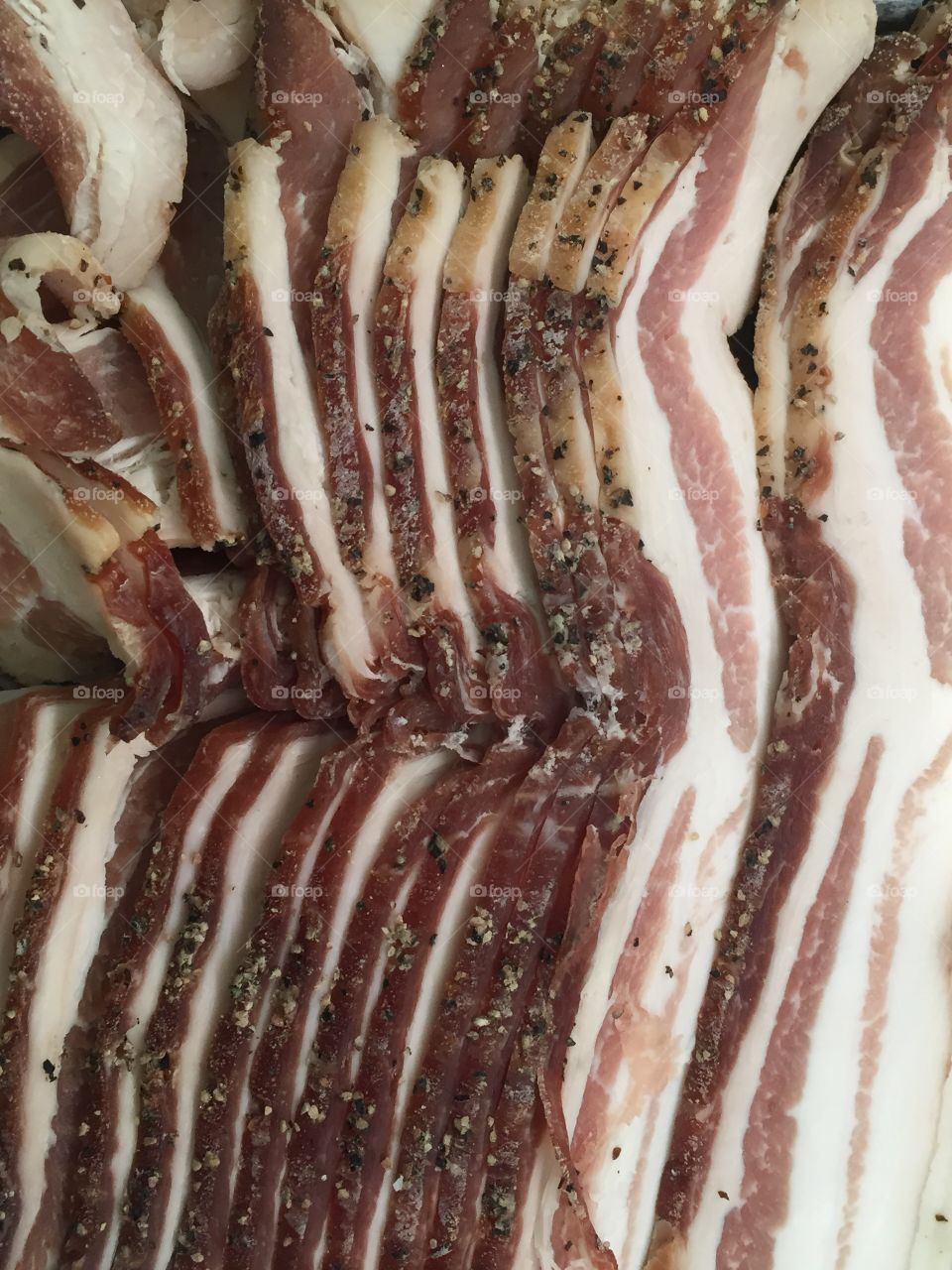 Closeup of uncooked strips of red, white, black and brown pepper bacon.