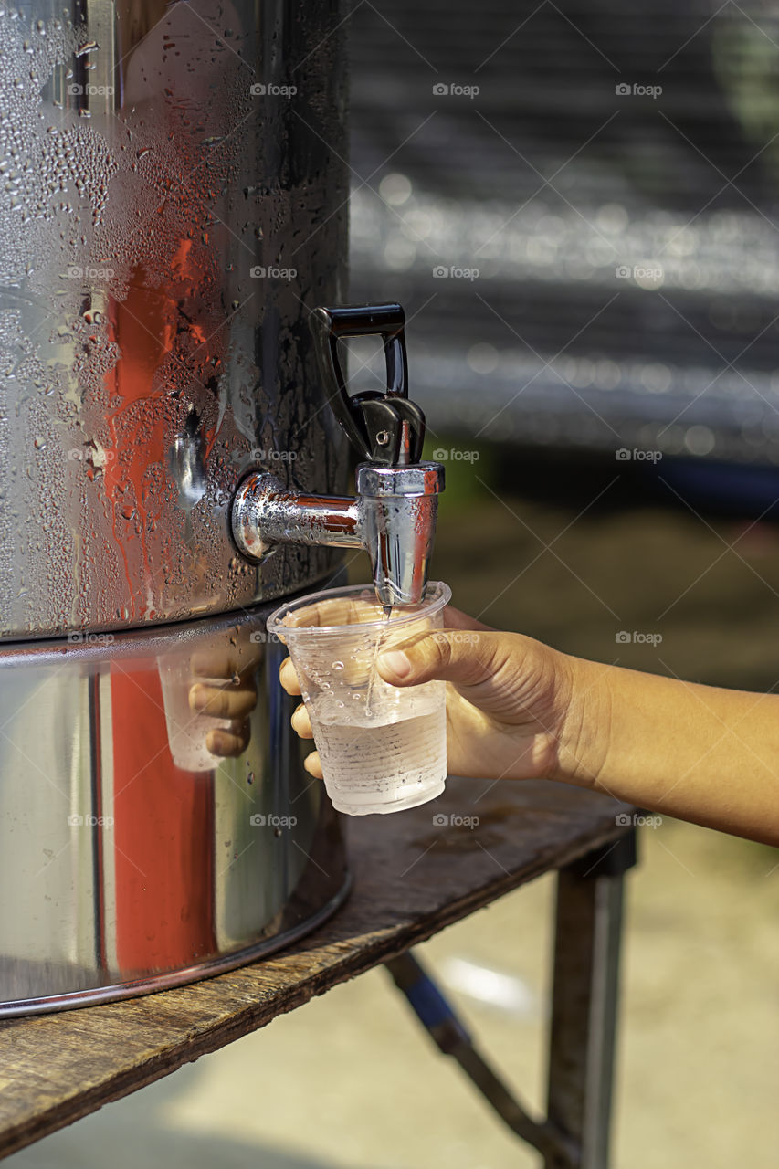 Hand boy holding the glass with water from the water cooler.