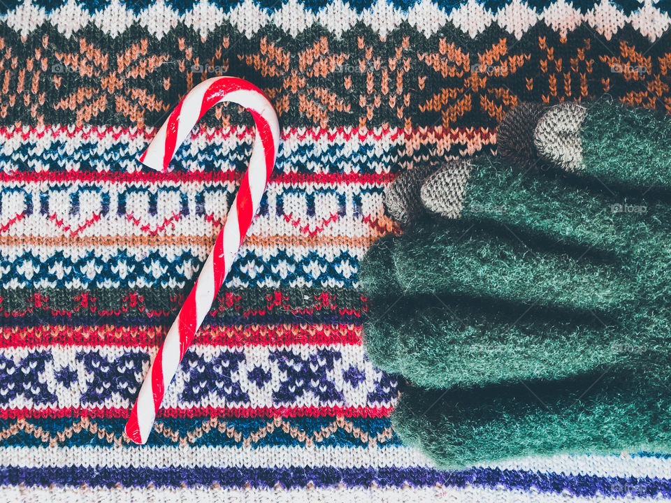 Green woolly gloves and a red and white candy cane on top of a patterned knitted jumper