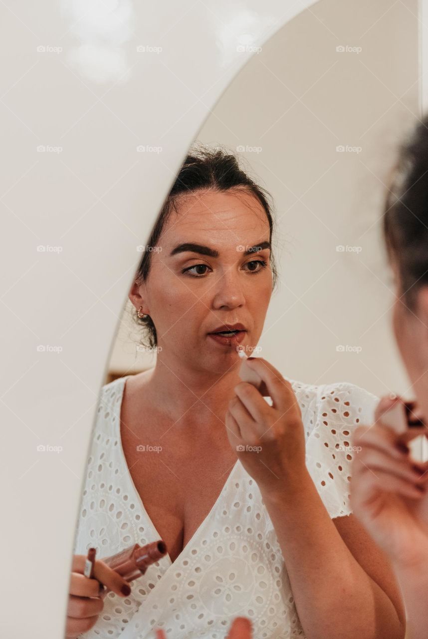 Mirror photo of young woman putting on lipgloss