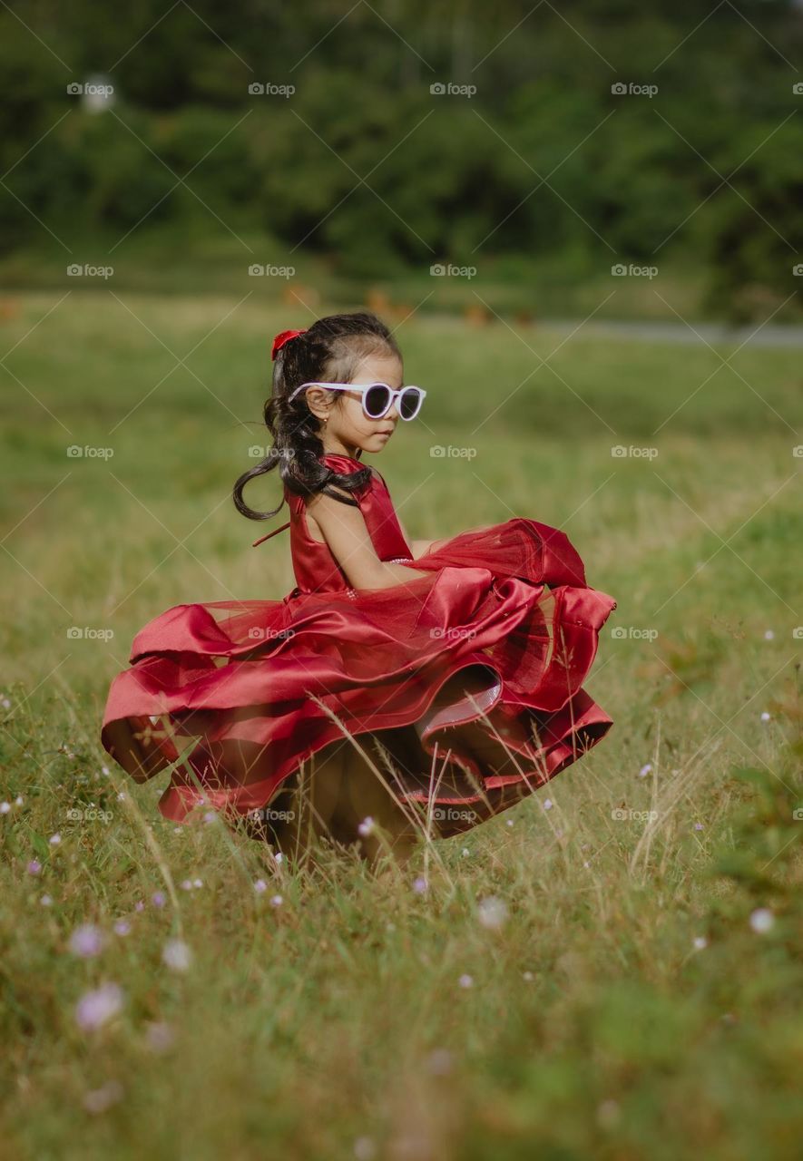 kid in red dress with sunglasses standing in nature park at summer