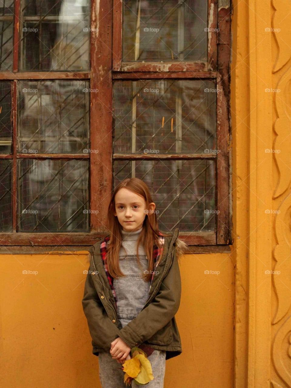A girl stands next to a window in an old yellow house