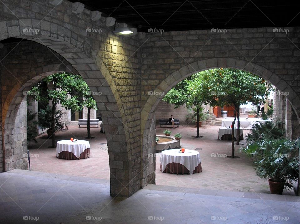 Tables in the courtyard of a restaurant under big old arch supports of a building