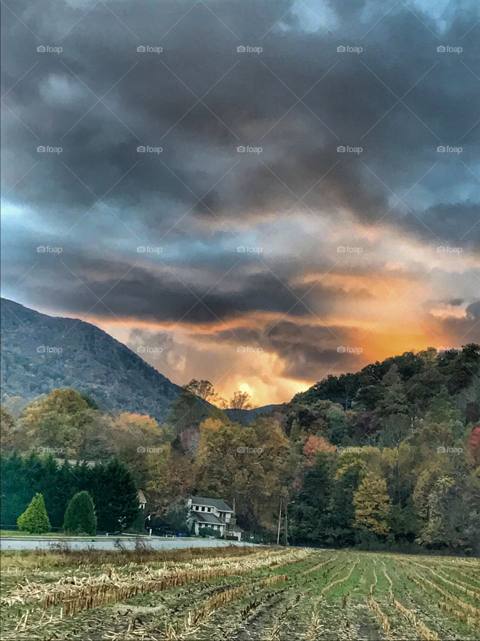 Sunset in a cloudy sky in the mountains seen across a harvested corn field 