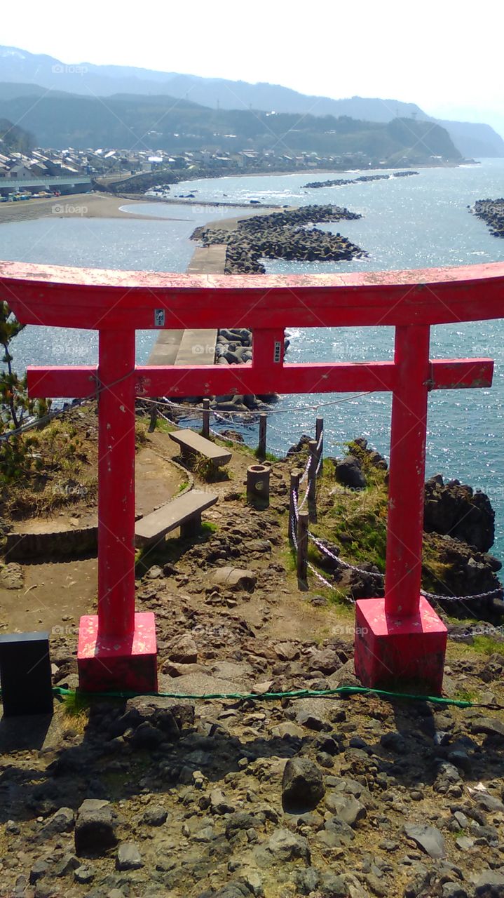A bright red gate frames the view of the sparkling waters as seen from Benten No Iwa.