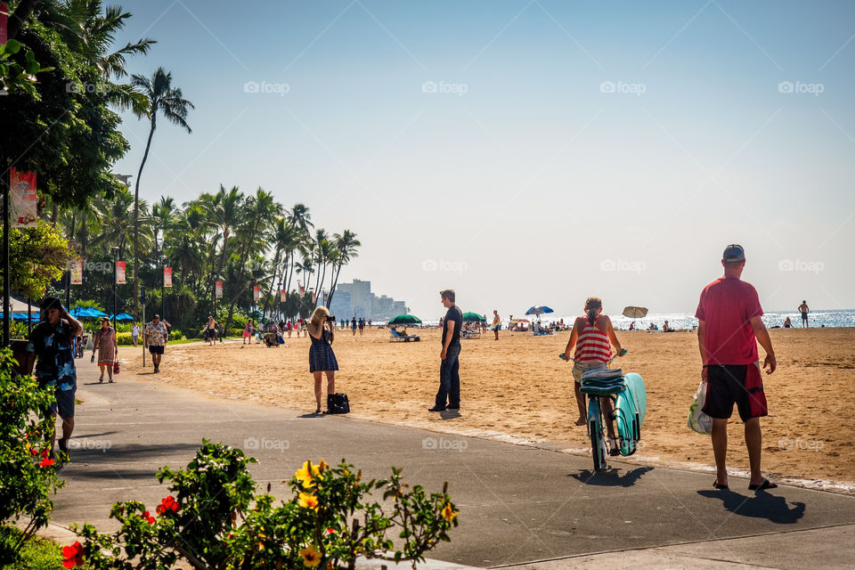 Waikiki, Honolulu, Hawaii, USA - December 13, 2015: The famous Waikiki Beach stretch and numerous visitors, with different activities on a cloudless, sunny afternoon. A sea spray gives the image a slight hazy look.