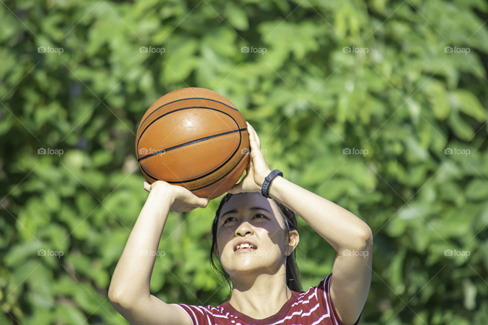 Leather basketball in hand of a woman wearing a watch Background blur tree in park.