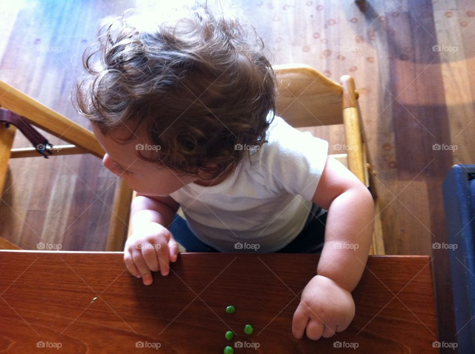 Baby in Restaurant. Chubby baby with curly hair in a restaurant sitting in a high chair eating peas.