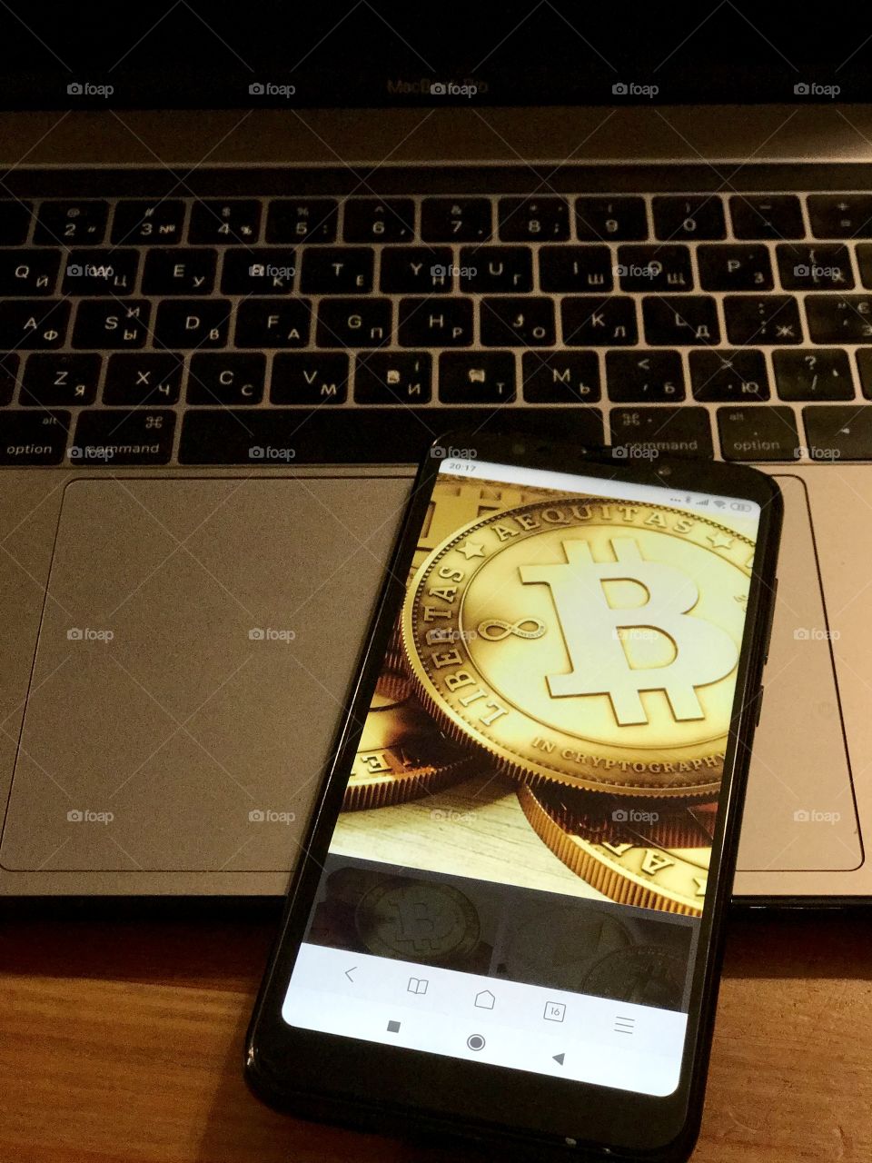 Mobile phone lies on the keyboard of the laptop, bitcoin symbols on the phone display.