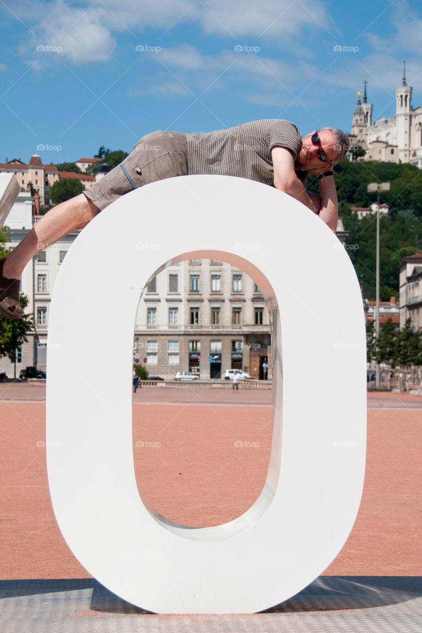 Man reclining atop the letter O in the family Lyon France sculpture