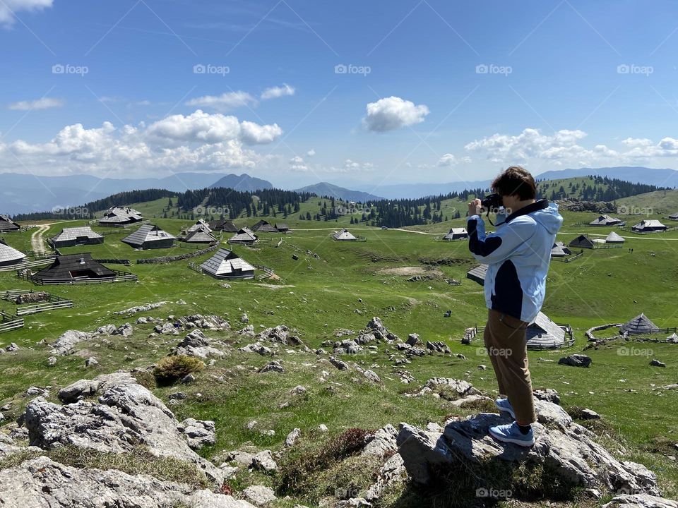 Backstage of the photo shooting in the beautiful Alps mountains in spring in Slovenia. Young woman photographer doing photos on her phone, camera