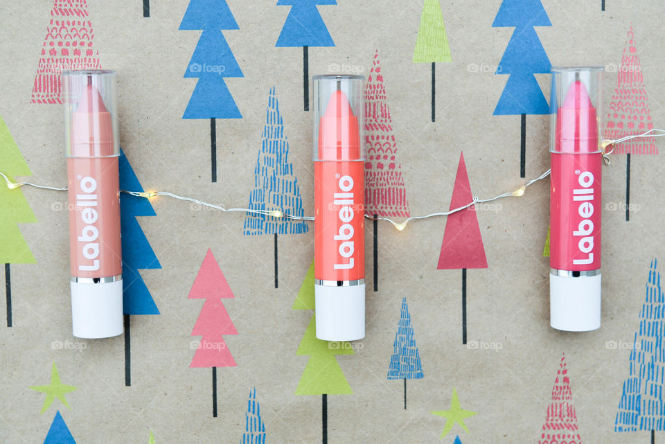 Row of Labello lip crayons and string of holiday lights on holiday tree wrapping paper