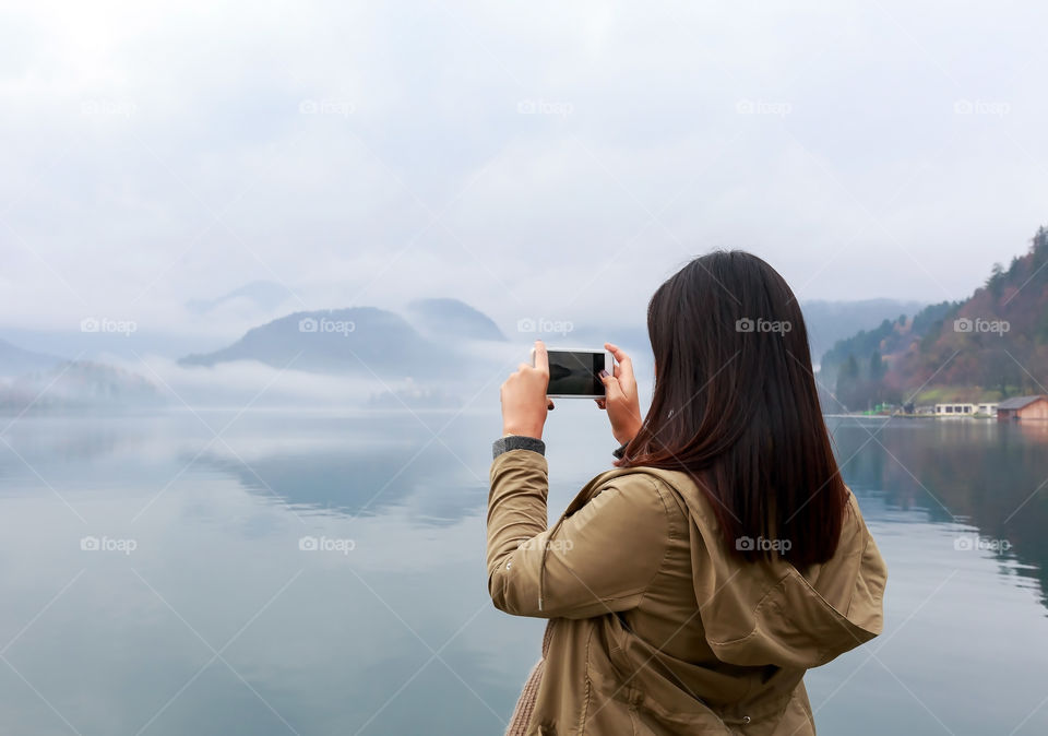 Rear view of a woman photographing calm lake