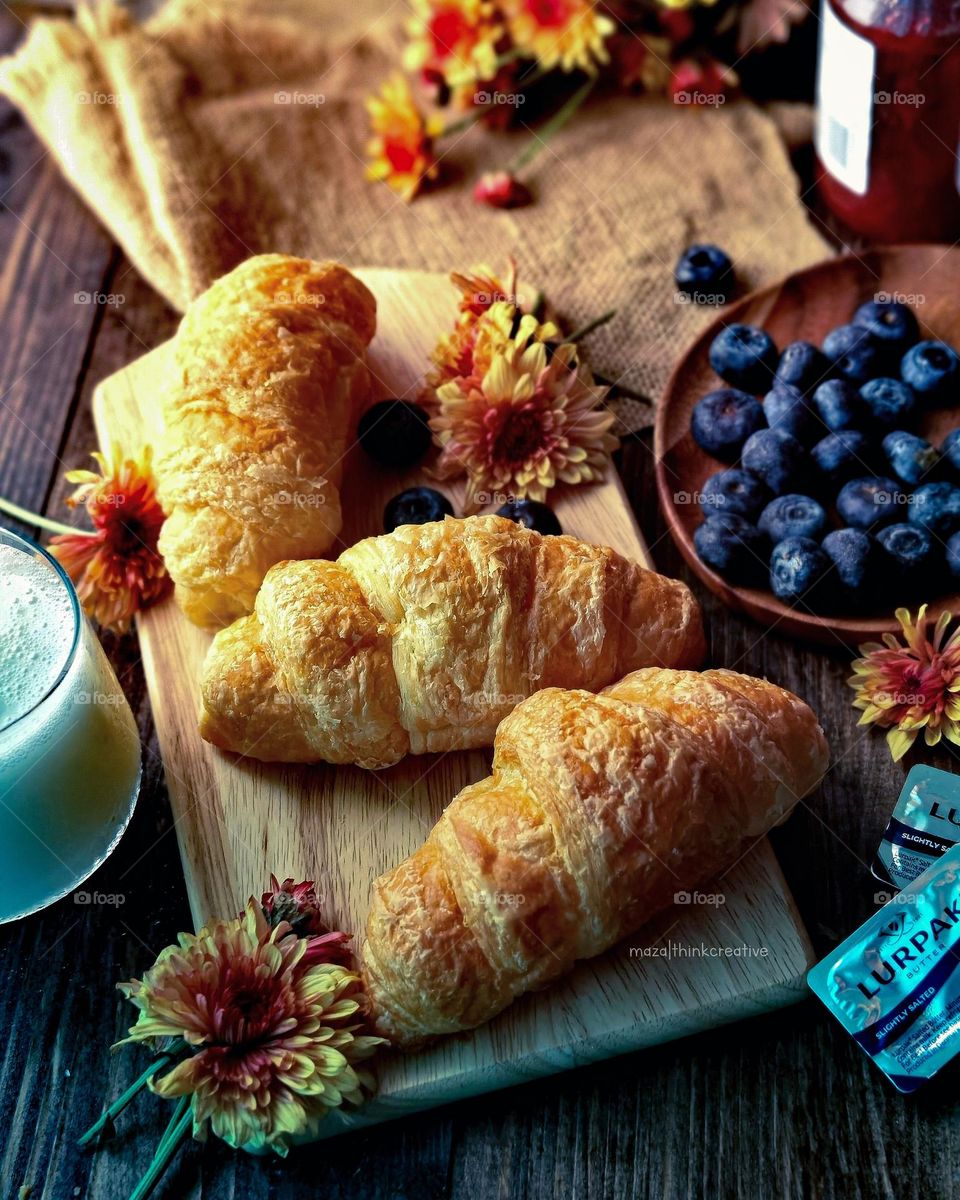 some croissants and fresh blueberries and a cup of milk beside it