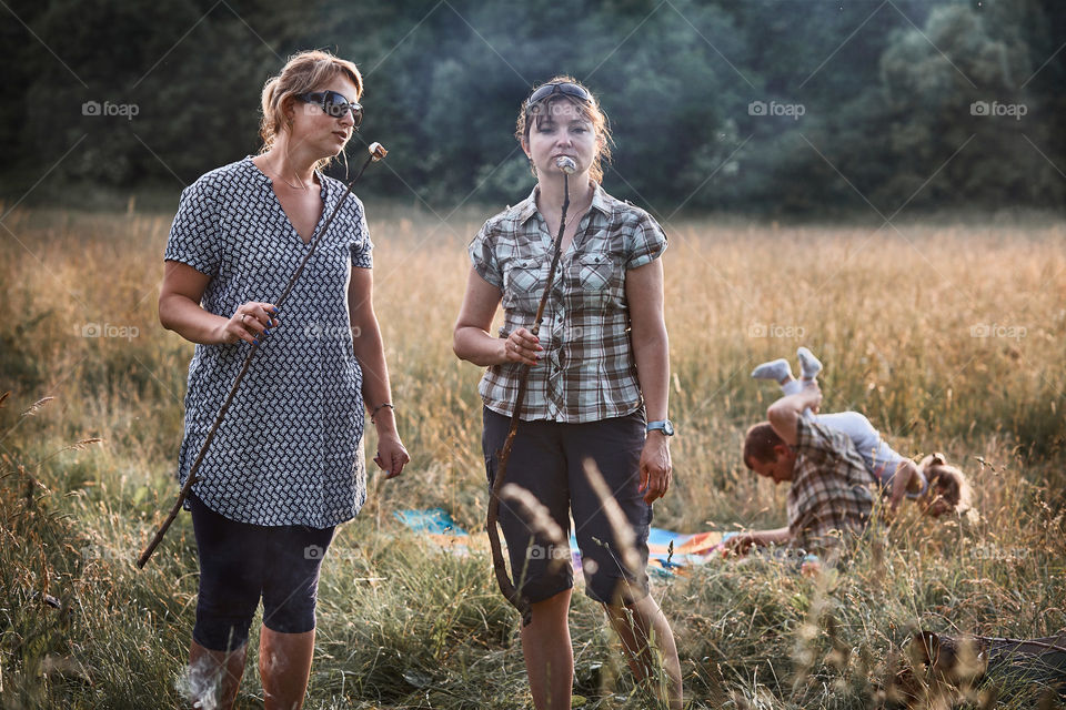 Women roasting a marshmallows over a campfire on meadow. Vacations close to nature. Candid people, real moments, authentic situations