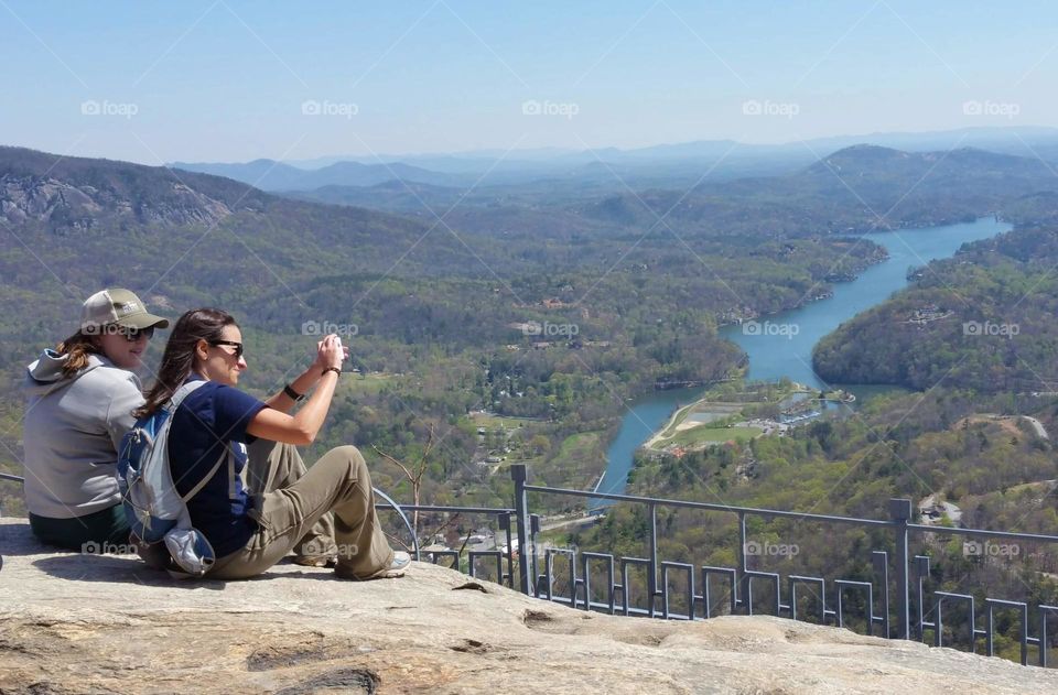 two women are taking a photo of the beautiful scenery from the top of a mountain overlooking a lake and valley