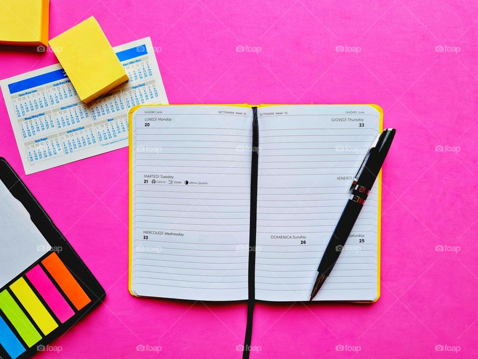 open agenda and office accessories on a fuchsia pink background