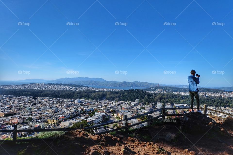 A man capturing the view of the San Francisco skyline, Golden Gate Bridge and more from the top of the Moraga Stairs in San Francisco, Ca.