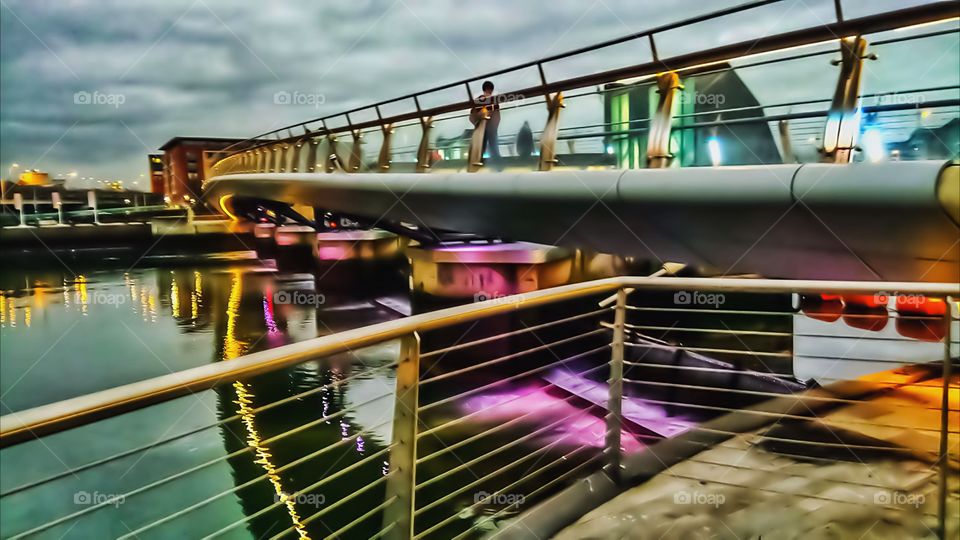 A bridge casts reflection on the calm waters in dusk light under a cloudy sky. Belfast,Northern Ireland