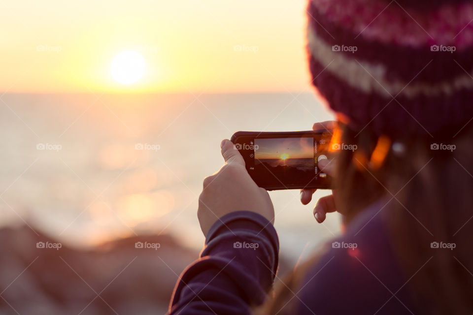 Woman using cellphone to take pictures of sunset 