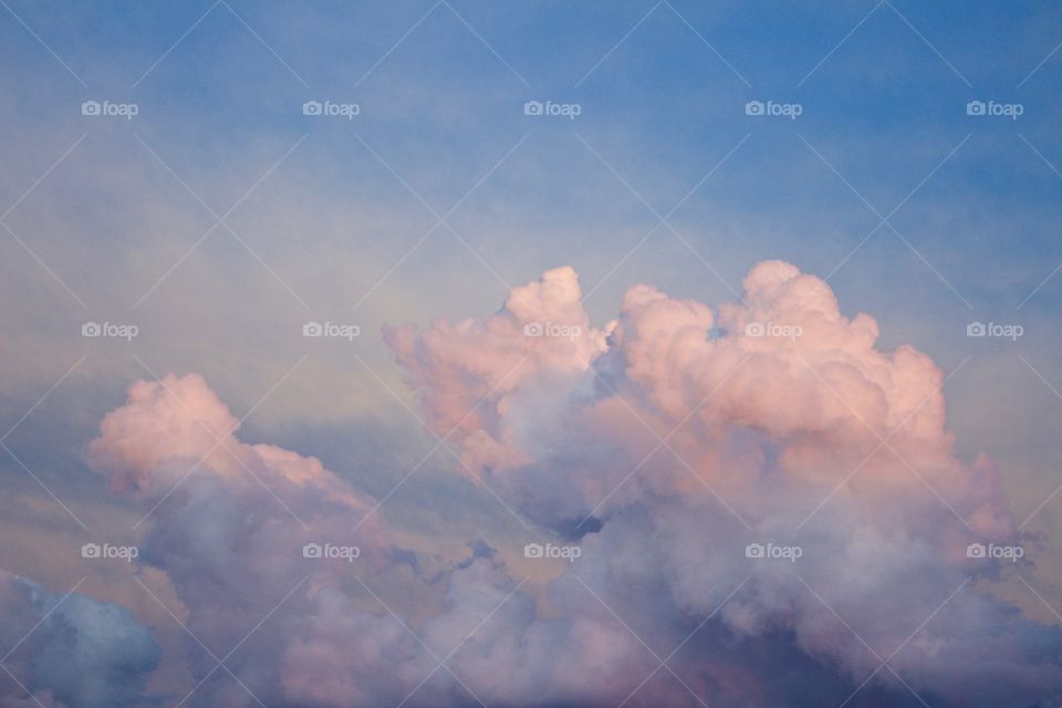 Pastel-colored clouds towering in the sky illuminated at the tops by low-angled sunlight