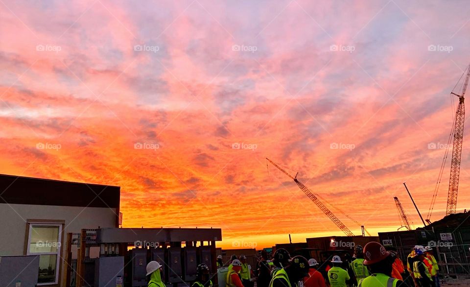 Crowd of United carpenters getting ready for another exciting day of work early in the morning and blessed by a majestic orange sky illumination the sky and the clouds above them.