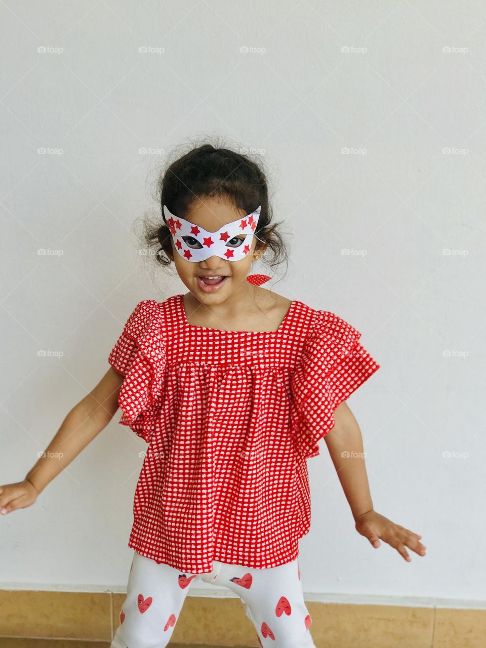 A cute little girl having fun with hand made red and white combination party eye mask.