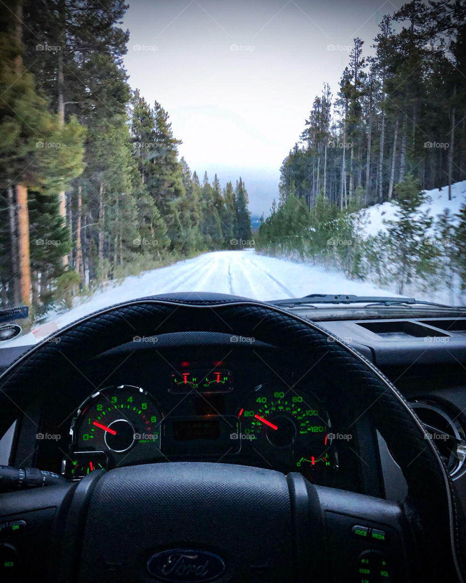 Driving on snow covered mountain roads surrounded by pine trees.