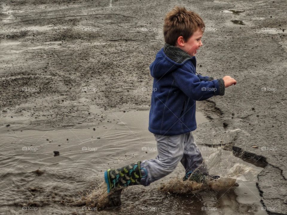 Boy Splashing In A Puddle. Child On A Rainy Day
