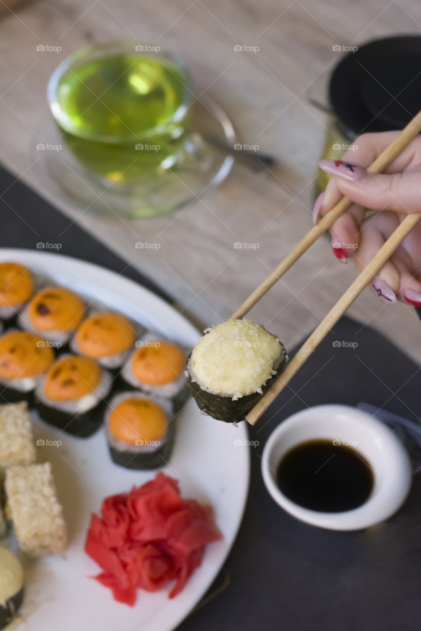 Woman holding sushi with chopsticks over plate of sushi. Young woman eating sushi sitting at table in restaurant, close-up