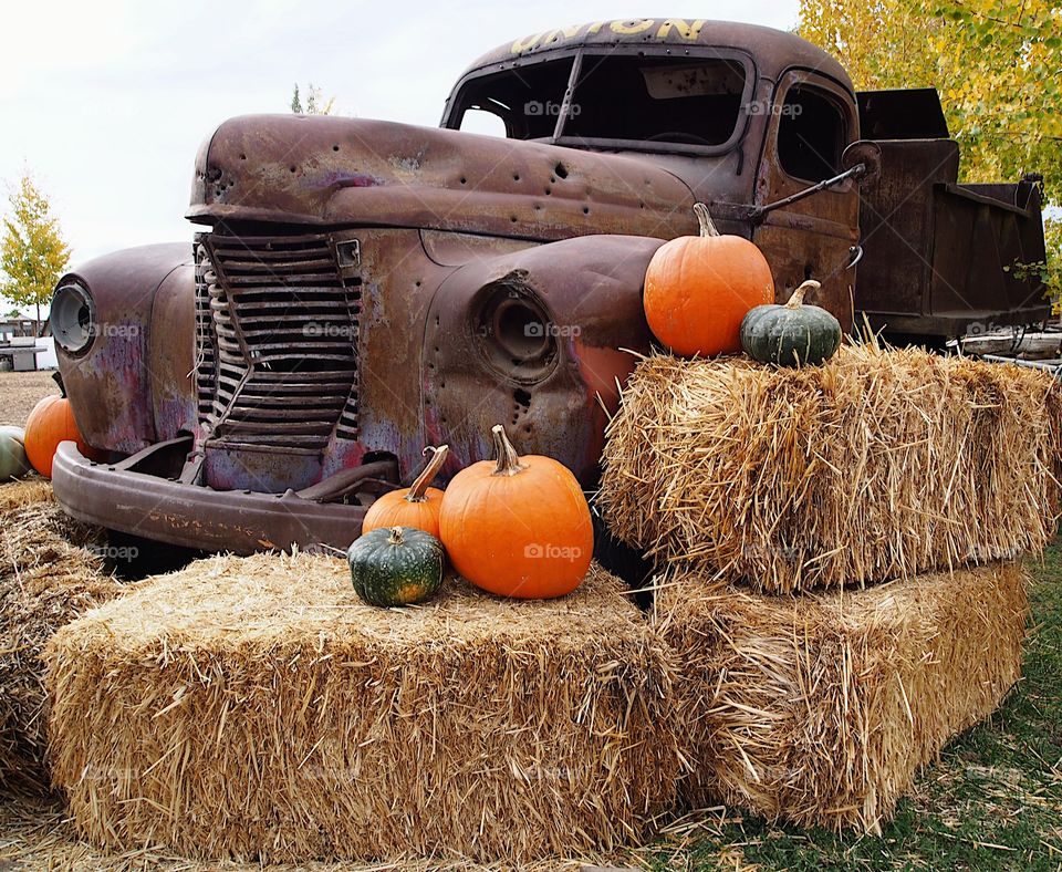 An old rusted truck that’s been shot up a little with hay bales and pumpkins in the foreground on a fall day in Central Oregon. 
