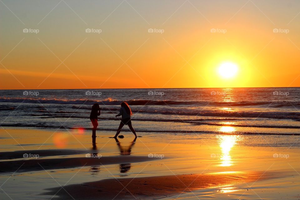 The silhouette of two children playing in the shoreline at dawn. 