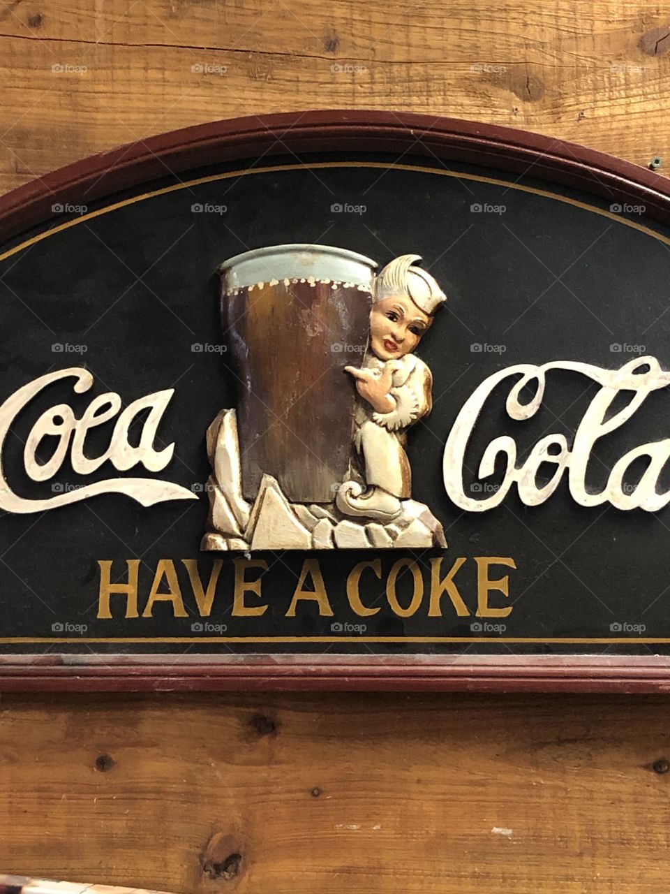 An old vintage Coca Cola sign showing the black background , white letters a glass of coke with little caricature. . 