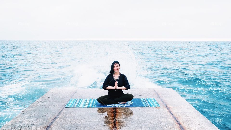 Woman in sports clothing practicing yoga and meditation on pier seaside in bad rainy weather 