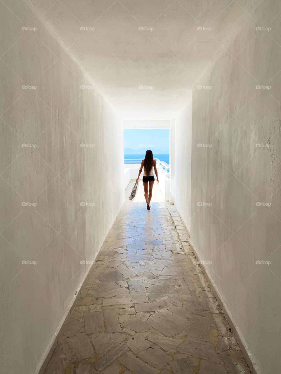 Silhouette of a young woman walking by the white corridor to the blue sea 