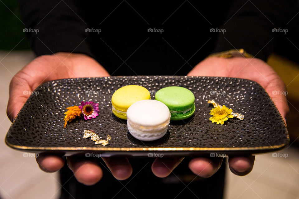 Colorful delicious sweet macaroon cookies served on a black plate. Biscuits on a plate held by a person.