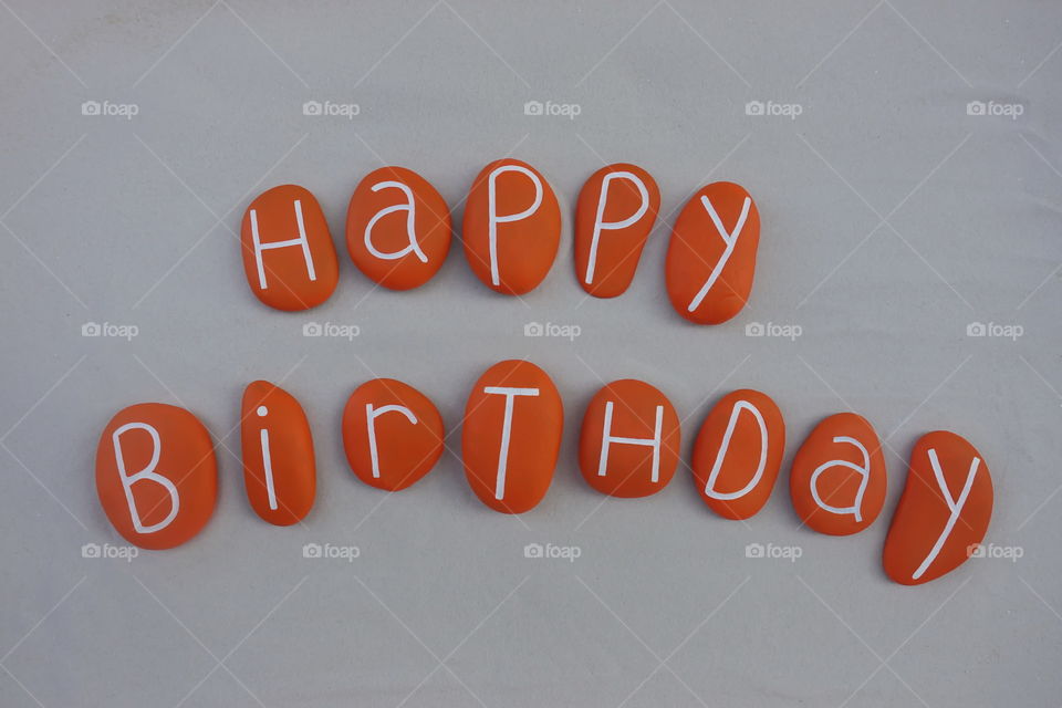 Happy Birthday text with orange colored stones over white sand