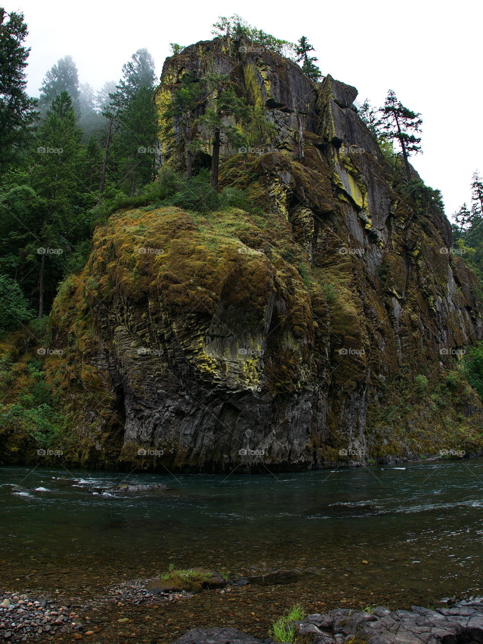 Boulders and rocks line the river banks of the magnificent waters of the Umpqua River in Southwestern Oregon on a summer morning. 