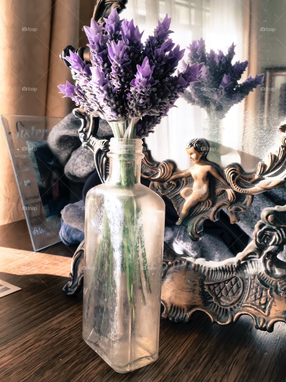 Bouquet posey of lavender in an antique medicine bottle sitting upon an antique wood dresser in front of an antique mirror, flowers reflected in mirror