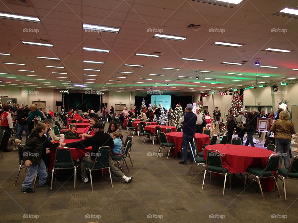 Tables full of people amongst the trees at a Christmas tree decoration event for charity. 