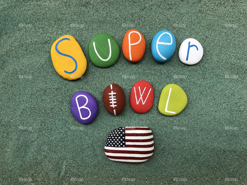 Super Bowl text with colored and carved stones over green sand