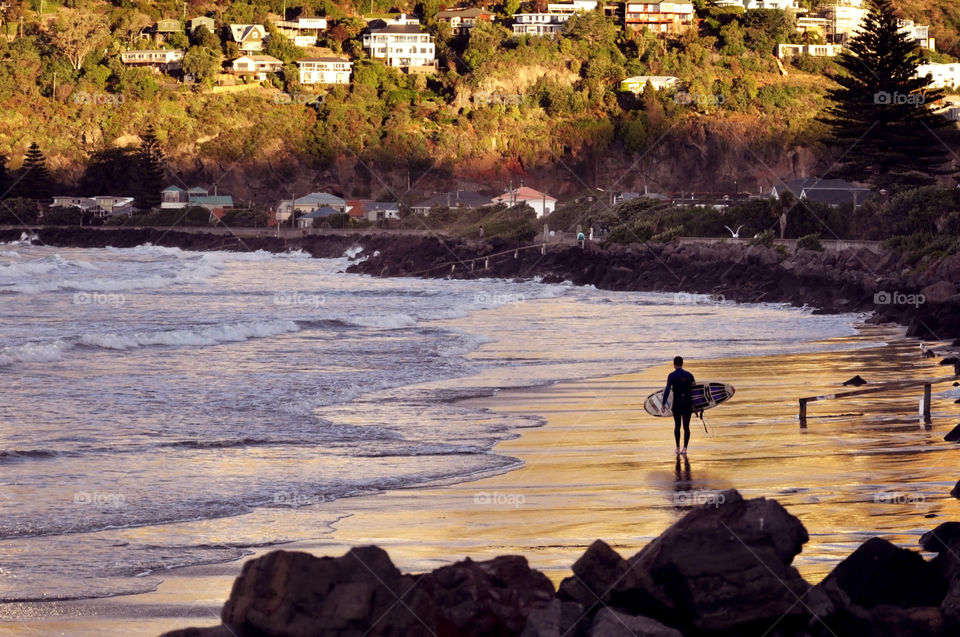 Rear view of man on beach with surfboard in hand