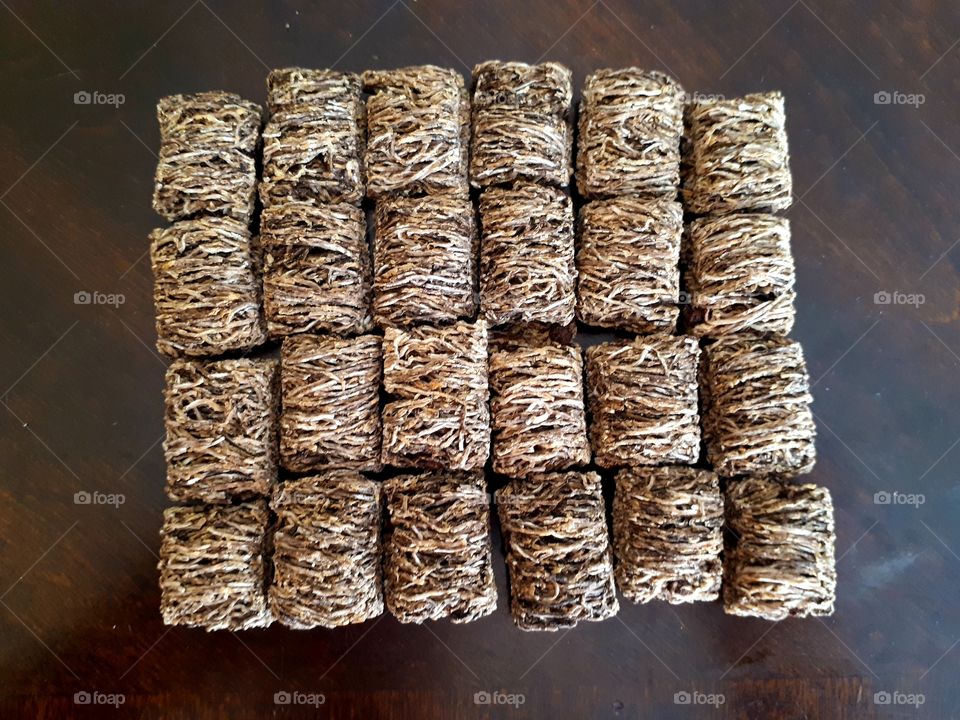 Twenty-four brown chocolate shredded wheat squares lined up in a rectangle on a brown wood laminate table.