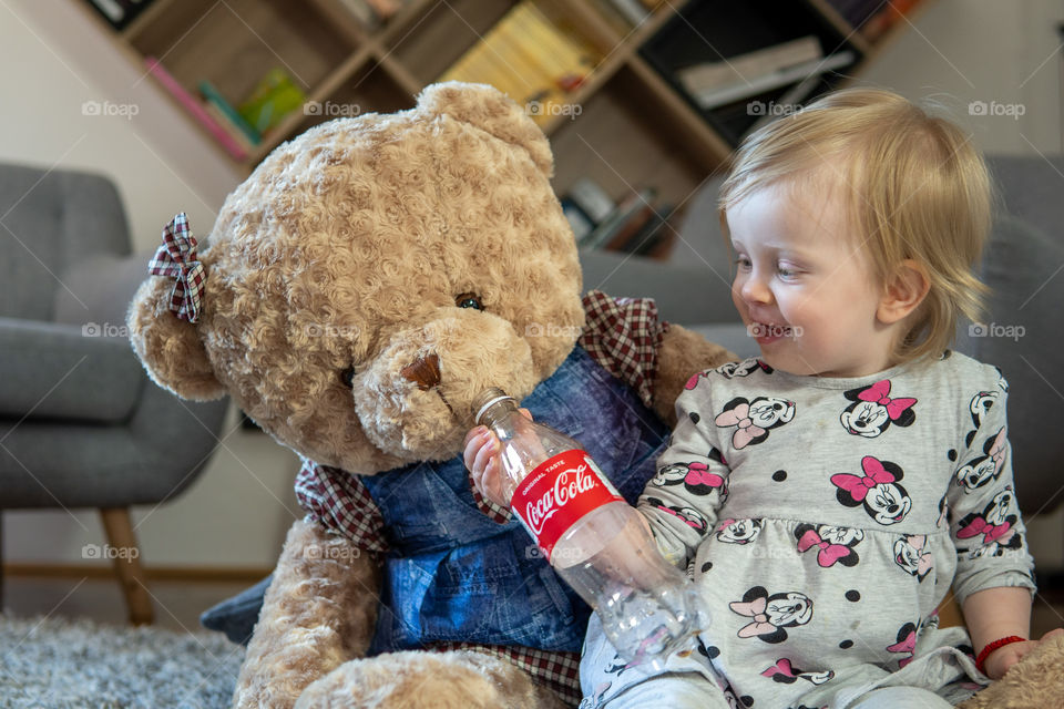 Baby girl giving last drops of coca cola to teddy bear